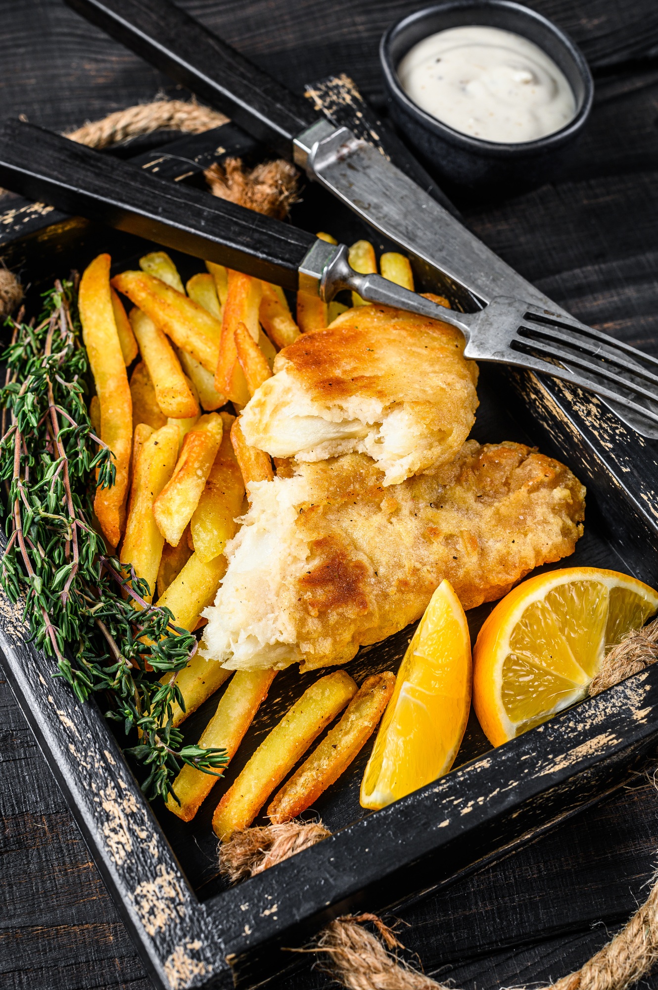 Battered Fish and chips dish with french fries and tartar sauce in a wooden tray.